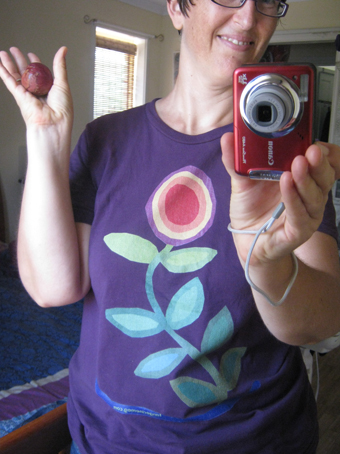 self portrait by and including my red camera, whilst also holding a plum and wearing a flower tshirt after my picture "Thriving"