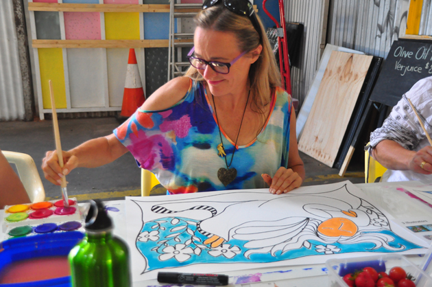 Happy, brightly dressed art student in brightly decorated old shed painting vibrant artwork at an art workshop