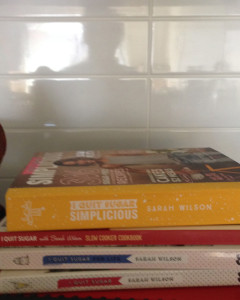 I quit sugar cookbooks in the foreground, with a reflection of me in the white tiles above