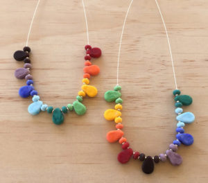 2 rainbow drop glass necklaces on wooden background
