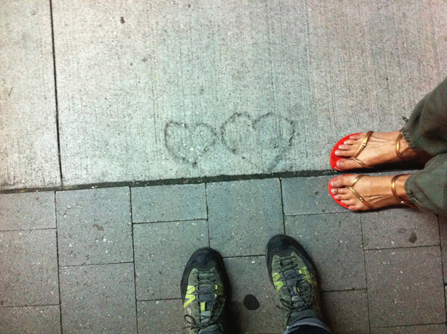 pair of feet in walking boots, pair of feet in sandals, standing on bricks and facing 2 hearts found in concrete