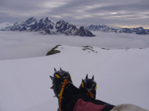 spikey shoe-d feet, crossed, with an outlook over NZ snowy mountain, Mt Cook