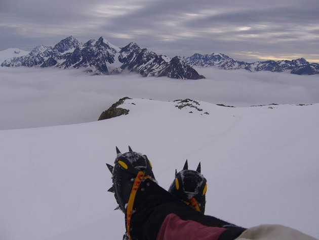 spikey shoe-d feet, crossed, with an outlook over NZ snowy mountain, Mt Cook