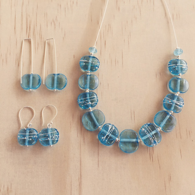 light blue glass necklace and earrings displayed on wood background