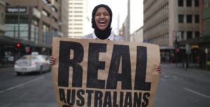 Happy women holding 'Real Australians Say Welcome' in a city street
