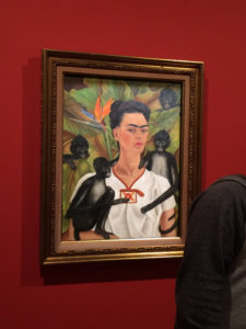 Frida Kahlo self portrait with monkeys, framed in gold and hanging on deep red wall