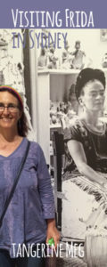 photo of Tangerine Meg smiling standing in front of big black and white photographic mural of Frida Kahlo in her art studio