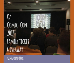 photo of convention room, showing audience heads chatting while they wait for a talk; on stage is a screen with the 2014 Oz Comic-Con logo of 2014; overlaid is blog post header in hand-writing looking font stating: " Oz Comic-Con 2017 Family Ticket Giveaway - Tangerine Meg". There's a purple border at the bottom and orange borders at the sides.