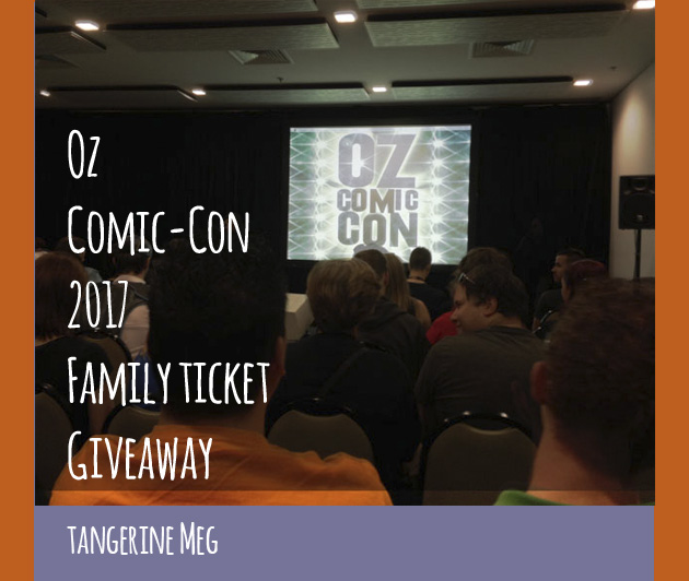 photo of convention room, showing audience heads chatting while they wait for a talk; on stage is a screen with the 2014 Oz Comic-Con logo of 2014; overlaid is blog post header in hand-writing looking font stating: " Oz Comic-Con 2017 Family Ticket Giveaway - Tangerine Meg". There's a purple border at the bottom and orange borders at the sides.