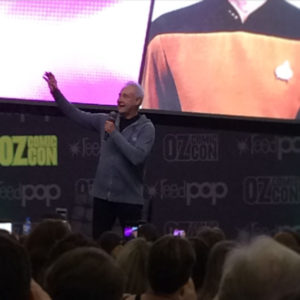 An Oz Comic-con audience is watching a man gesturing on stage. The background is a cropped Star Trek uniform.