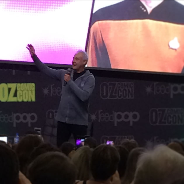 An Oz Comic-con audience is watching a man gesturing on stage. The background is a cropped Star Trek uniform.