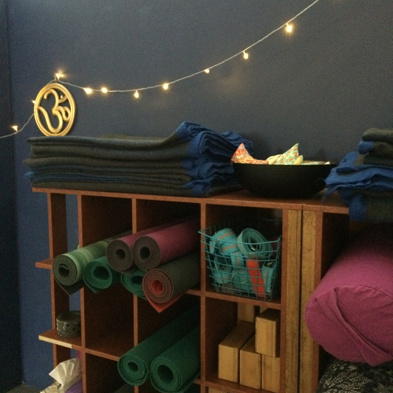 bolsters, blocks and other yoga equipment neatly stored under the OM sign and fairy lights