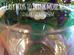 A glass with water and light reflected in it, with pansies in the background adding colour