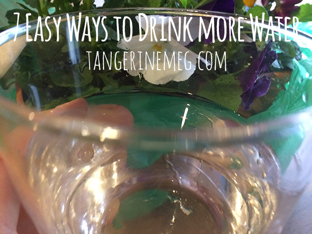 A glass with water and light reflected in it, with pansies in the background adding colour